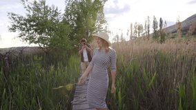 Steadicam shot of a happy beautiful girl running through the green bulrush followed by her boyfriend with camera. Slow motion.