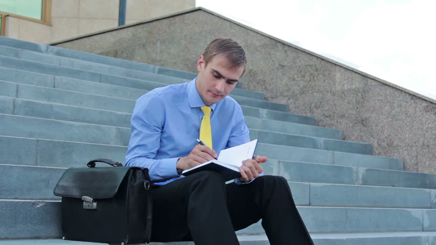 Young serious businessman writing on notepad and standing up