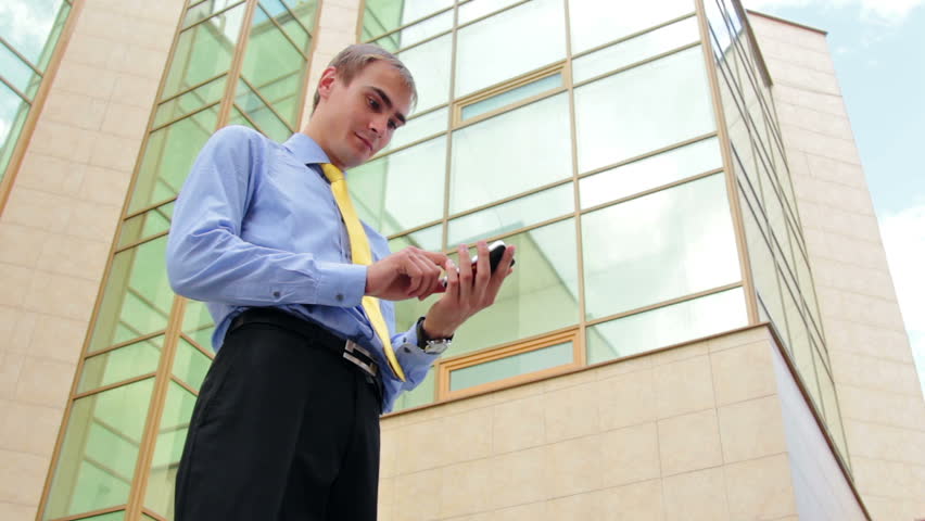 Successful businessman texting on cellphone near the office building
