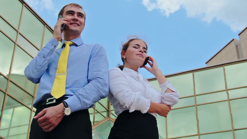 Businesswoman and businessman standing back to back and calling by cellphones