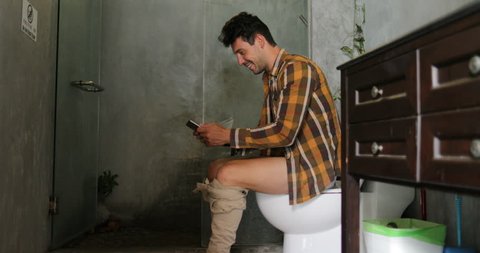 Man Sitting On Toilet Use Cell Smart Phone Young Guy Chatting Online In Restroom