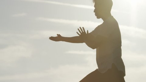 Male silhouette doing Tai Chi martial arts during sunset