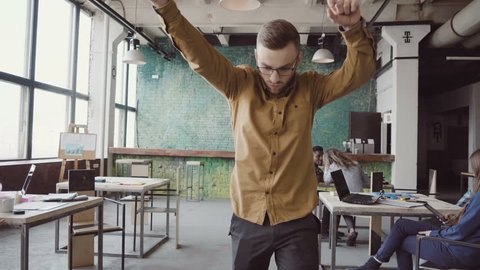 Handsome young businessman doing victory dance about successful achievement. Happy male at modern trendy office.