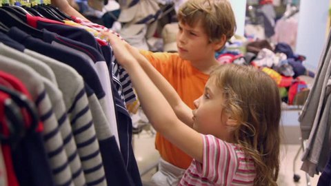Two kids boy with little girl take and watch shirts in clothes shop