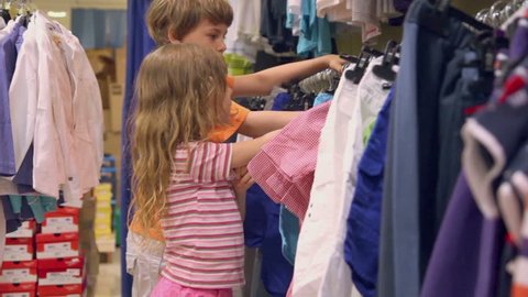 Two kids boy with little girl watch clothes and try on in shop