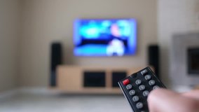 A man with a remote control from the TV switches channels on a large flat TV