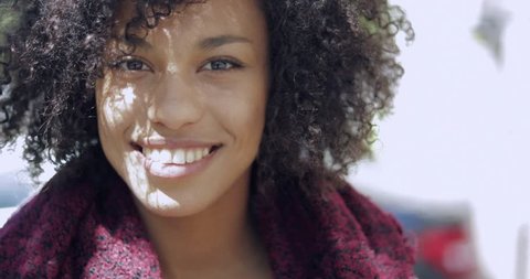 Portrait of young African woman with short curls smiling and looking at camera while standing on street in sunlight.