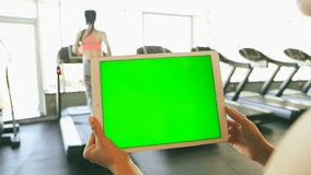 Hands holding tablet computer with green chroma key screen. On the background sport club with Treadmills and woman having running workout. video footage
