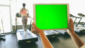 Woman using tablet pc with green chroma key screen inside sport club with runners on Treadmills. video footage
