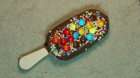 Rainbow Sprinkle Ice Cream Bar Melts into Puddle - Closeup of a chocolate ice cream bar with rainbow sprinkles melting into a puddle