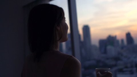 Happy woman drinking coffee and admire view during sunset by window
