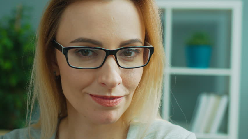 Portrait of young attractive business woman in glasses posing on camera, removing the glasess and smiling in office background. Close up.