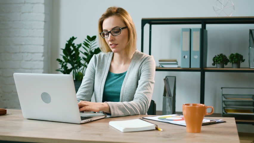 Young business woman talking with friend on skype using her laptop in office background. Attractive woman speaking with business partner using skype on laptop.