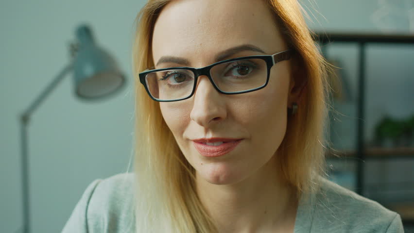 Portrait of attractive business woman in glasses posing on camera, smiling on office background. Close up.