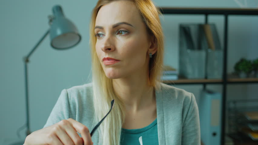 Portrait of attractive business woman holding the glasses, posing and smiling on camera in office . Close up.