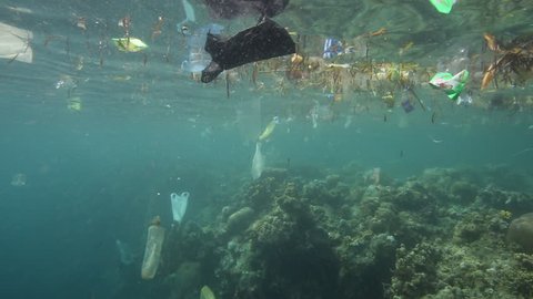Plastic garbage and other trash floating underwater over fragile coral reef