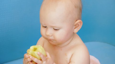 Baby eats peeled apple holding it in both hands