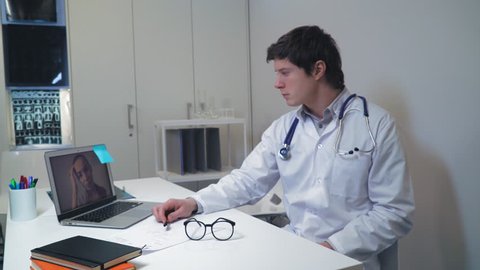 Doctor talking with patient using application on laptop. Therapist has online meeting with unhealthy woman. Physician sitting at the desk in office use internet.
