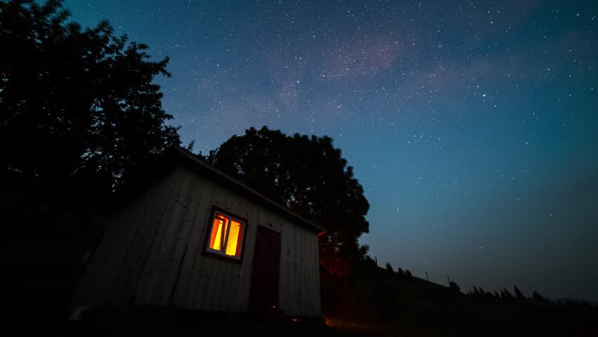 The Milky Way galaxy rotating over the rural cabin house in the mountains