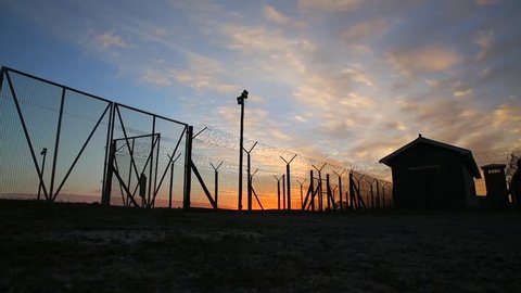 South Africa, Cape Town - May 31 2016: Robben Island Prison precinct, sunset Timelapse of sun setting and clouds moving overhead, Prison barbed wire fence silhouetted