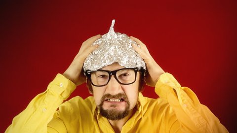 An angry ugly man wearing a tin foil hat (made from aluminium, worn in the belief or hope that it shields the brain from threats such as electromagnetic fields, mind control or reading).
