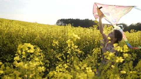 Sunset shot of cute teenager girl wears dress plays with flying colorful kite, runing on field of yellow flowers, freedom concept, 120FPS slowmotion