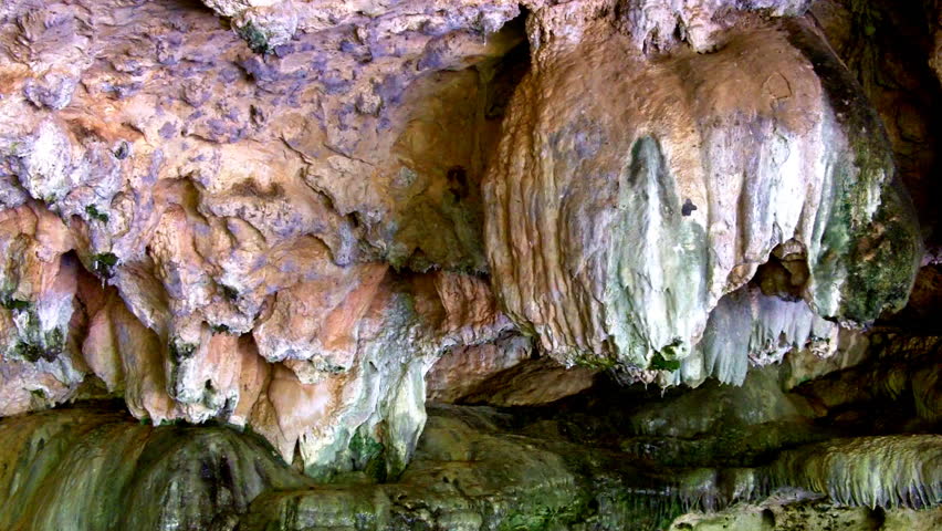 Spring water drips from colorful rock formations on the roof of a limestone
