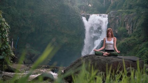 Woman doing yoga (Kapalbhati) in front of Tegenungan Waterfall, Ubud