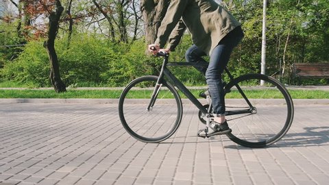 Tracking shot of hipster man riding fixed gear bicycle in park, slow motion
