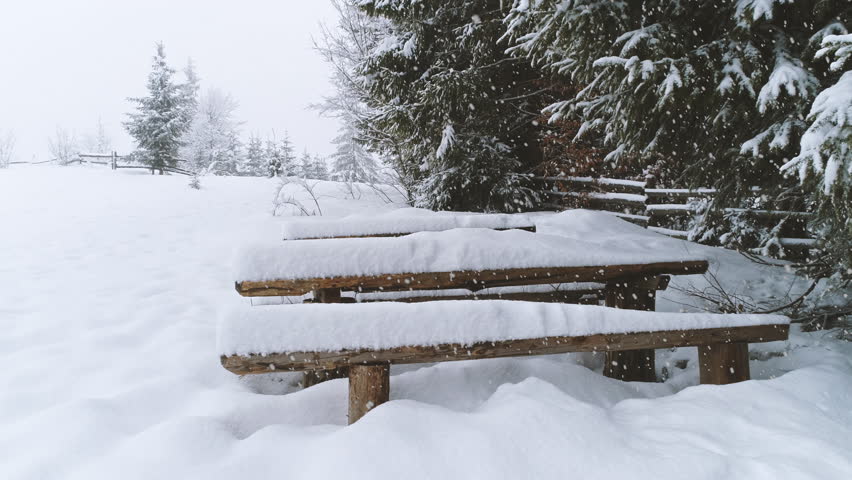 Bench covered in snow while more snow falls.