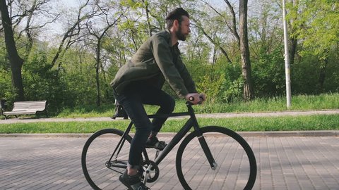 Tracking shot of hipster man riding fixed gear bicycle in park, slow motion