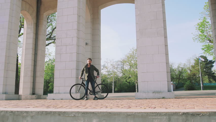 Hipster man sitting on his fixed gear bicycle in park near the gate