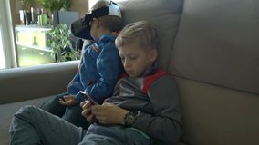 Two boys with vr goggle and smartphone sitting on sofa at home
