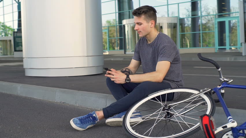 Man sitting on the border scrolling websites and fixes his hair slow motion