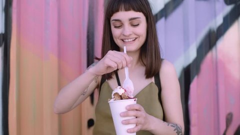Cute fashionable woman snacks on sweet delicious dairy free fruit berry ice cream with a tiny spoon. She truly enjoys the food dessert on outside party