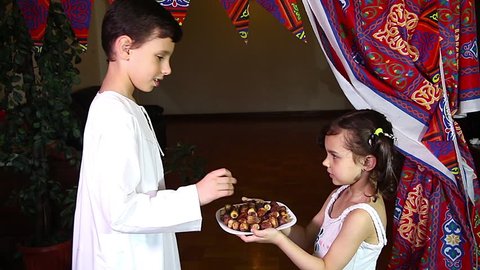 Little Muslim girl presenting a dish of dates for iftar to little muslim boy - breaking fast in Holy Ramadan  - showing generosity of Ramadan