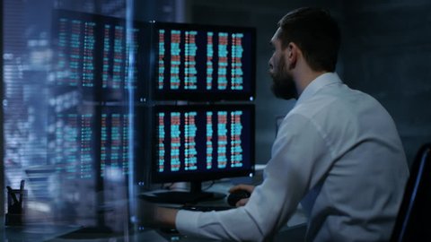 Late at Night Trader Reads Numbers on His Multiple Displays with Stock Information on Them. In Background Big City Window View. Shot on RED EPIC-W 8K Helium Cinema Camera.