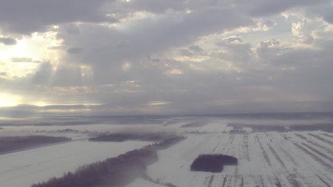 Over frozen prairie and woodland in Quebec, Canada, sun rays through clouds