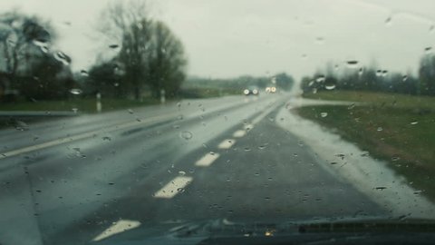 Rain is pouring on car glass - automobile windscreen wipers sweep water drops away. Focused on glass.