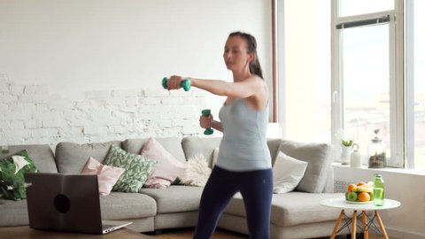 young fit woman warm up doing sport exercises with weights online using app on laptop computer for healthy lifestyle at home during sunny day