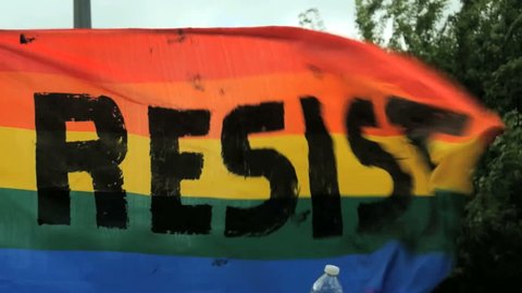 Resist sign banner Rainbow flag waves in the wind blowing during activist rally gathering.  Activism slow motion LGBTQ gay pride civil rights climate march