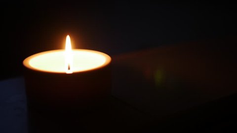 Close-up of a match lighting a candle against a wall background, shallow depth of field with focus on the wick and flame.