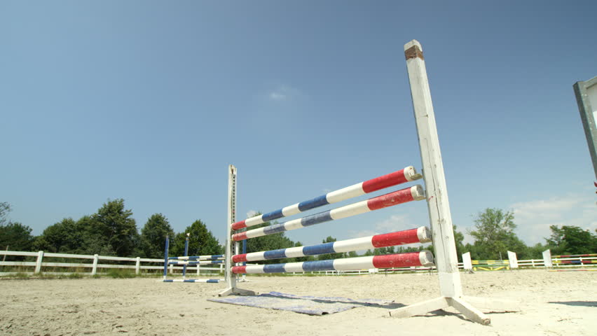 SLOW MOTION, CLOSE UP, LOW ANGLE: Woman riding beautiful chestnut mare jumping the fence in sunny outdoor parkour arena. Horse with a female rider training for the open jumping competition in manege Royalty-Free Stock Footage #26911432