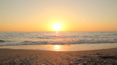 Sunset on the beach - Tranquil idyllic scene of a golden sunset over the sea, waves slowly splashing on the sand