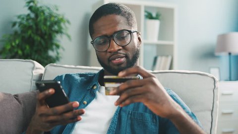 African young man in glasses shopping online with credit card using smart phone at home. Indoor.Isolated,  Quarantined  concept  isolation  home, protection , Ordering food delivery , paying order