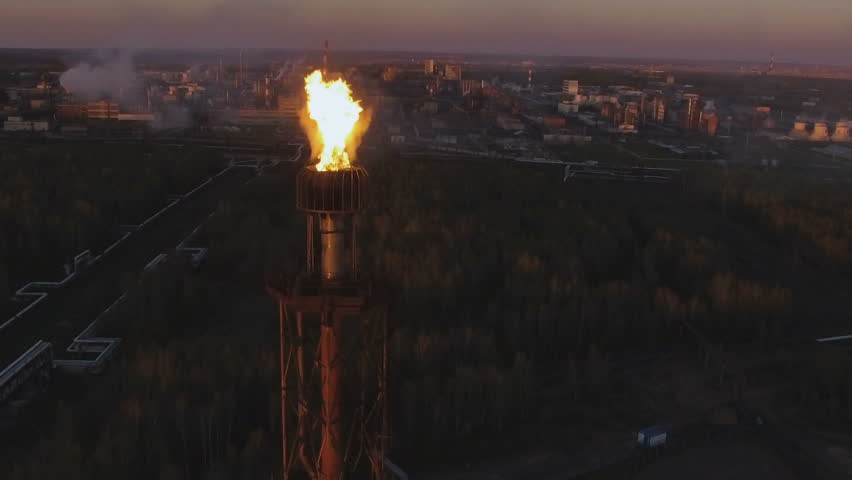 a tower with a torch on an oil refinery among the woods at sunset. Aerial view