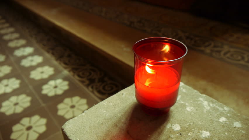 Illuminated candle in a church with an old floor in the background