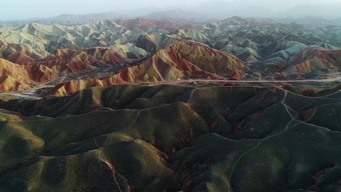 Approaching one of the most beautiful rainbow mountains in Zhangye National Geopark, part 3 of a continuous 3 part series. Aerial view on grass-covered sandstone hills in front of a colorful mountain