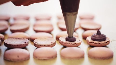 cooking, food and baking concept - chef with confectionery bag squeezing cream filling to macarons shells at pastry shop