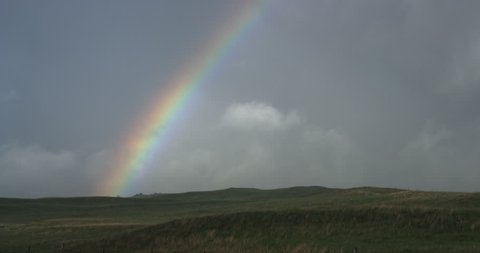 A rainbow in a cloudy gray sky over rolling green hills